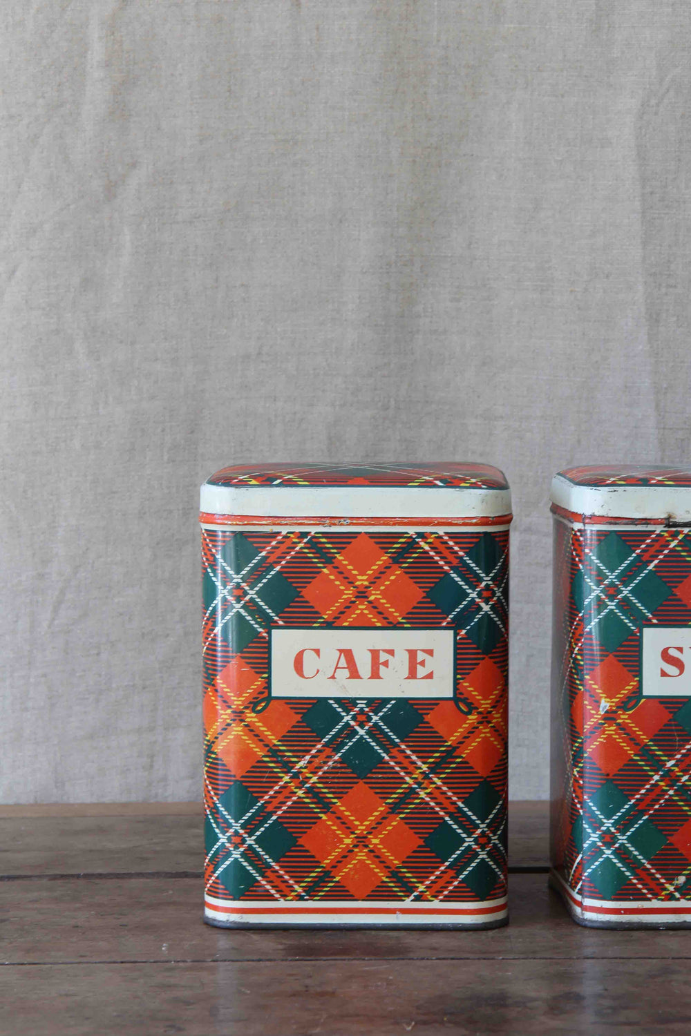 Two vintage-style metal canisters with plaid patterns and 'CAFE' labels on a wooden surface.