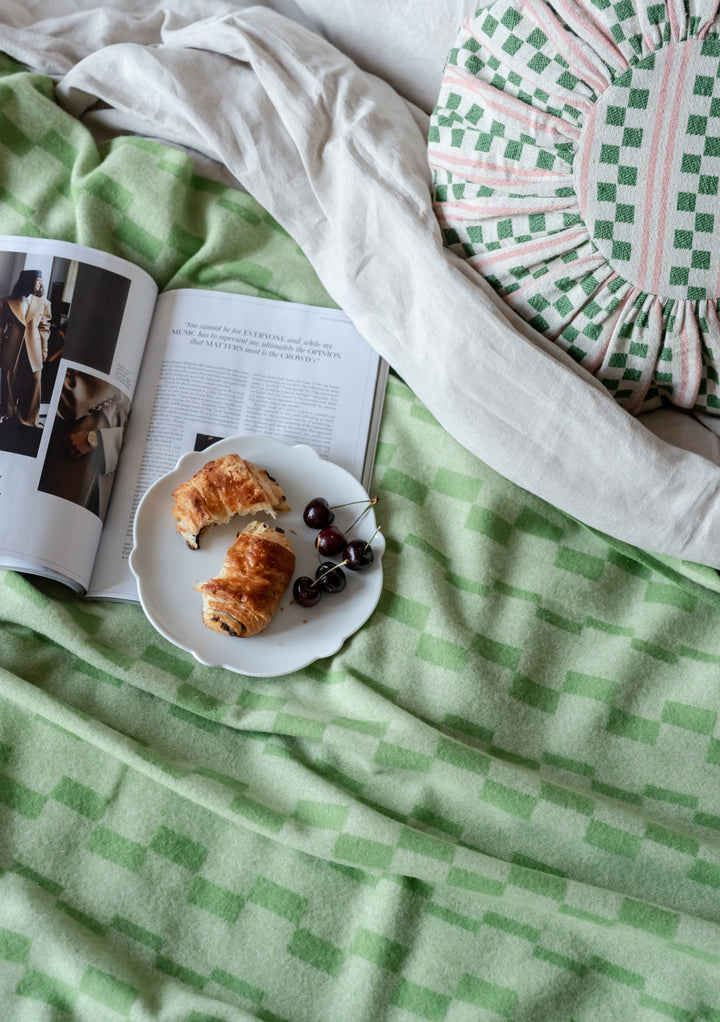 green and pink patterned circular cushion on ruffled green bedspread with breakfast plate