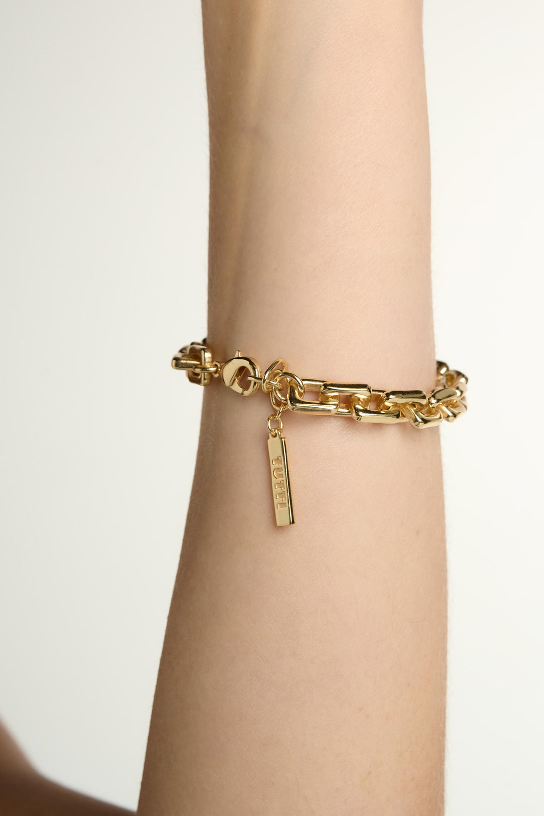 Gold chain bracelet on a wrist with a plain background