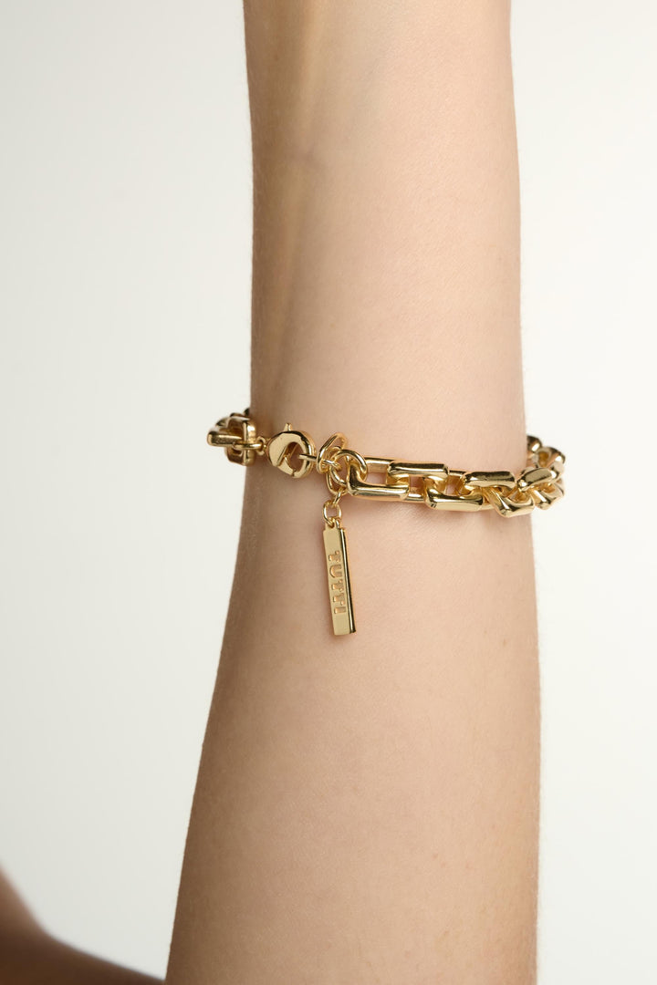 Gold chain bracelet on a wrist with a plain background