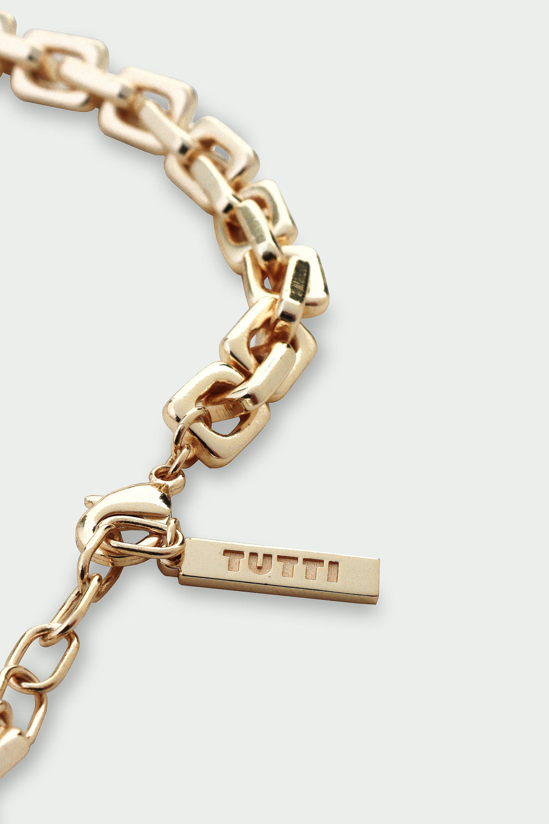 Gold chain bracelet with a visible brand tag on a light gray background