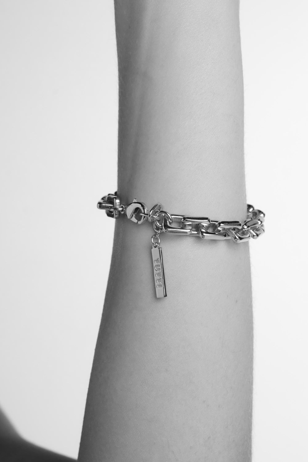 Silver chain bracelet with a tag on a wrist against a white background