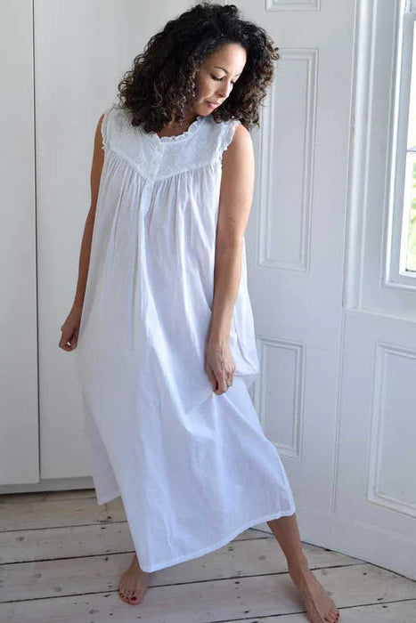 Woman wearing a white dress standing in a bright room with a window in the background.