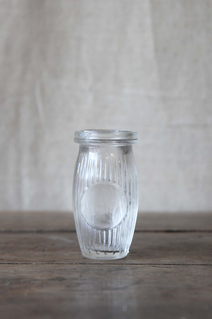 Clear glass paste jar with ribbed design on a wooden table and beige background