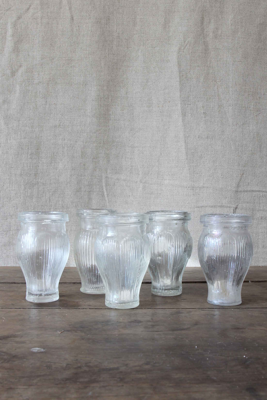 Set of five ribbed glass vintage paste pots on a wooden surface with a textured beige background
