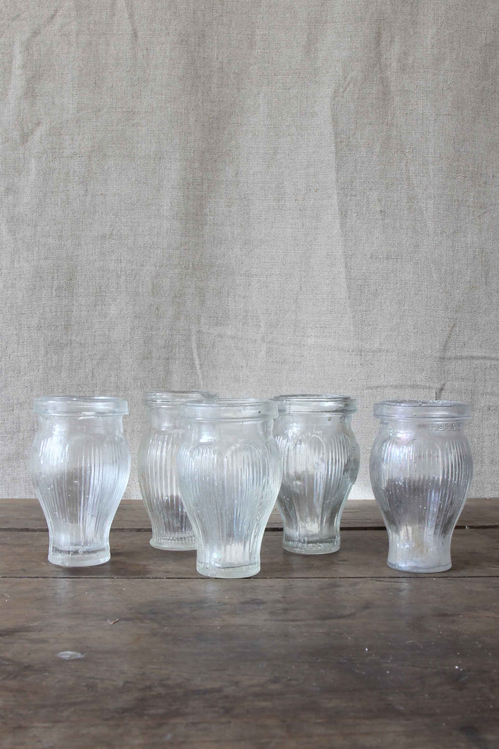 Set of five ribbed glass vintage paste pots on a wooden surface with a textured beige background