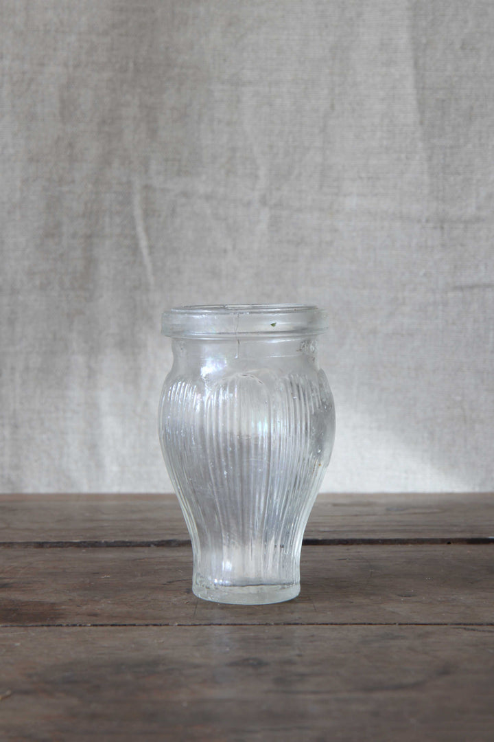Clear glass vintage paste pot with ribbed texture on a wooden surface with a beige fabric background
