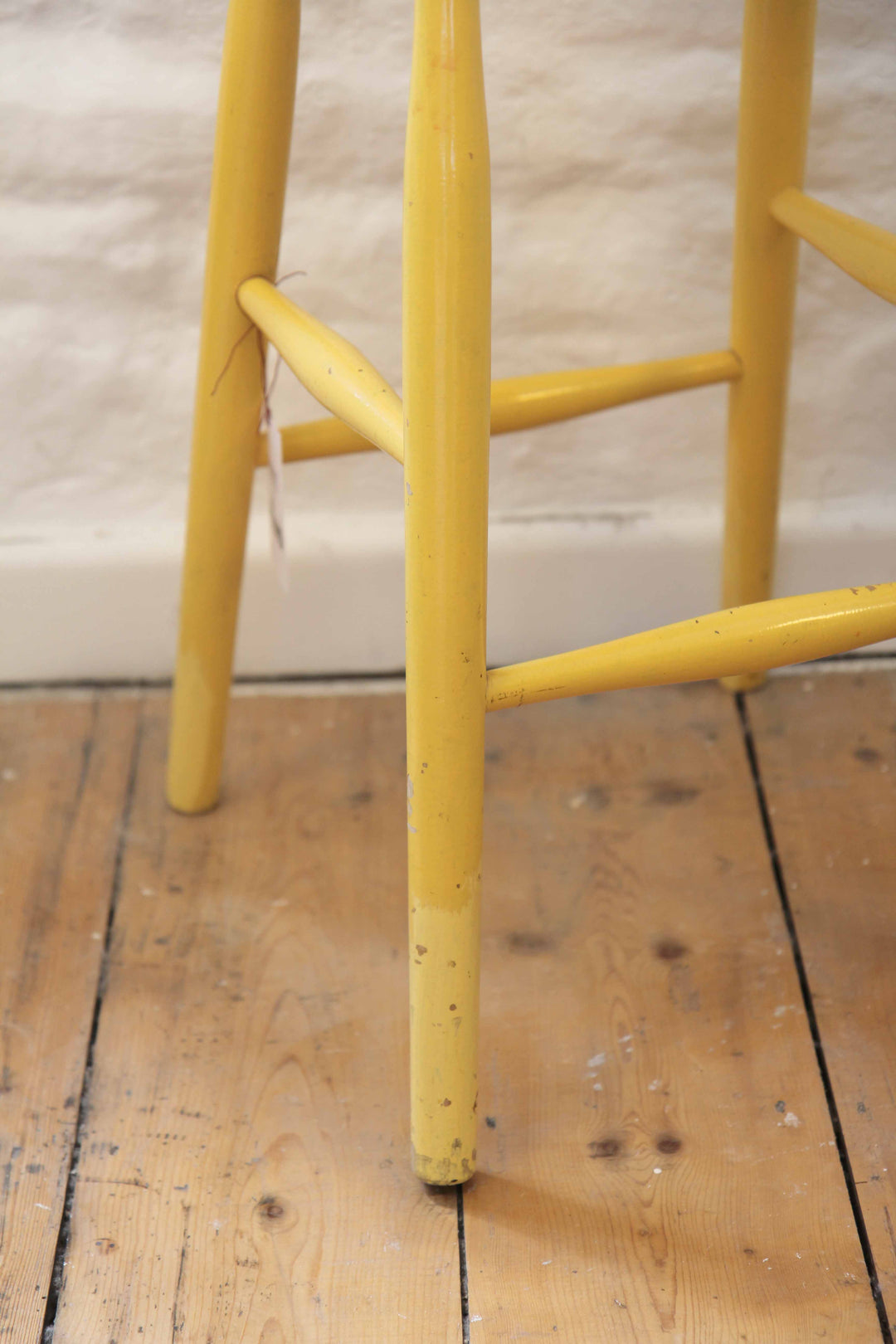 Yellow metal bar stool on a wooden floor with a neutral wall background