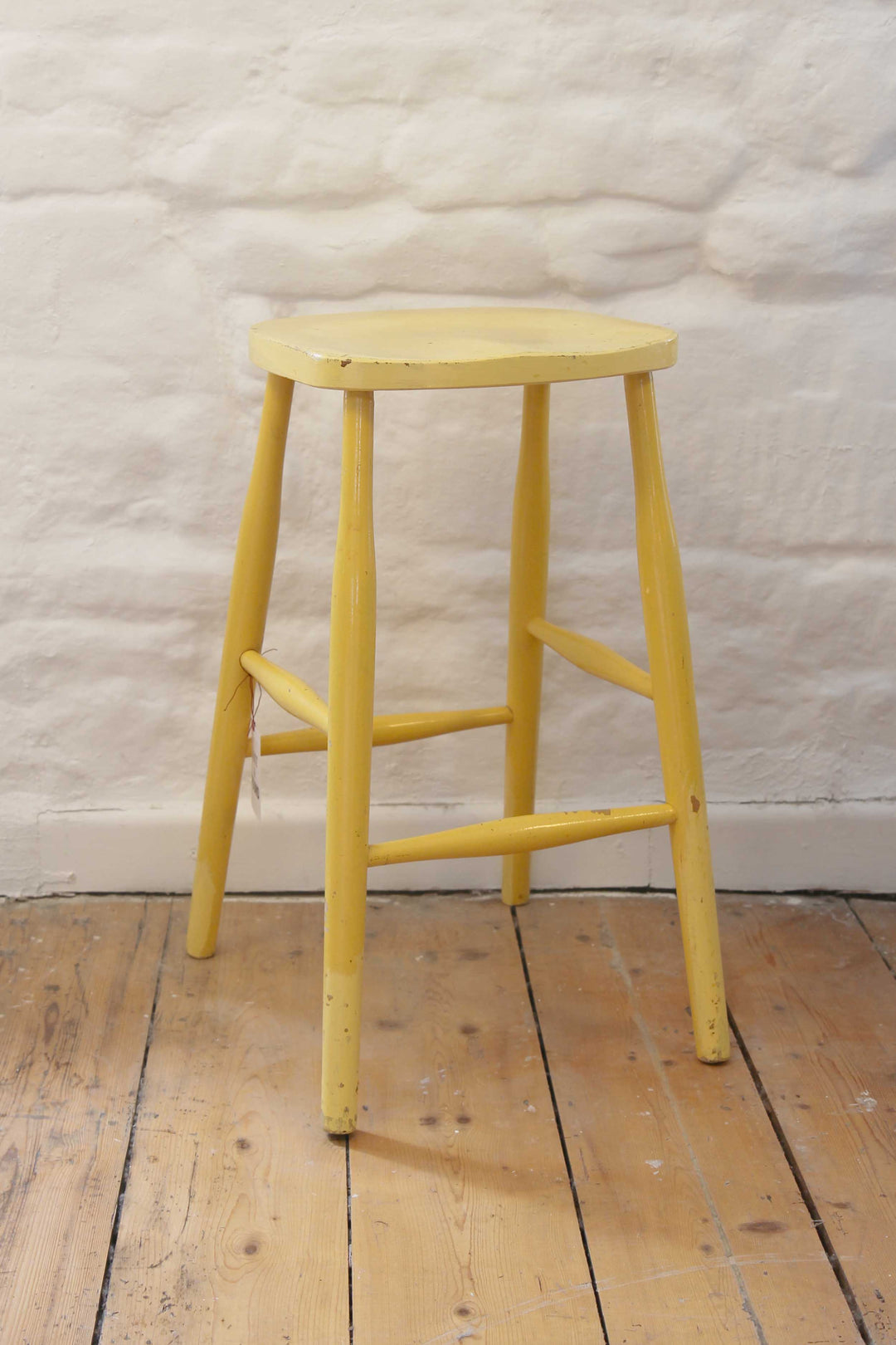 Yellow wooden stool on a wooden floor with a textured white wall background