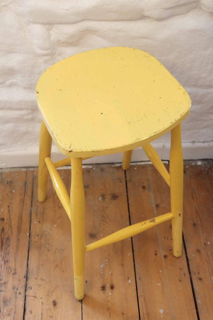 Yellow stool on a wooden floor with a textured white wall background