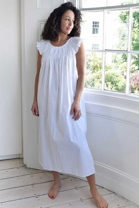Woman wearing a white dress standing in a bright room with a window.