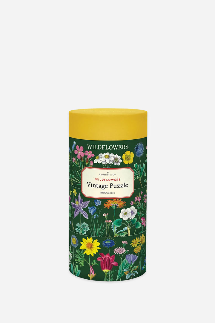 A cylindrical puzzle tin with a yellow lid and a dark green floral label reading &