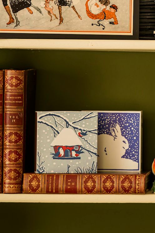 Decorative books and framed artwork on a shelf against a green wall.