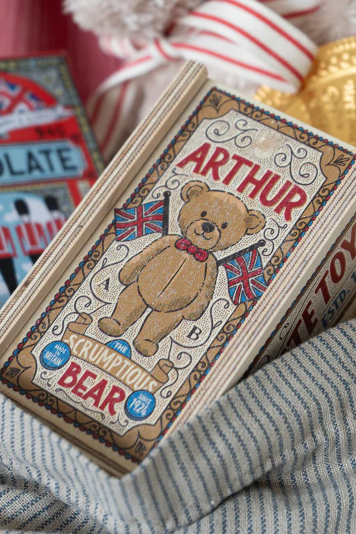 Cardboard box with a teddy bear design and 'Arthur' text, featuring British flags, on a textured surface.