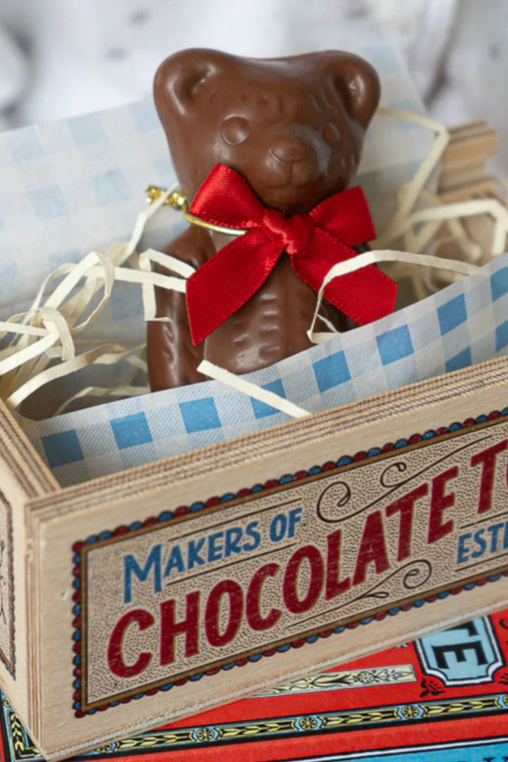 Chocolate bear with a red bow in a decorative box labeled 'Makers of Chocolate'.