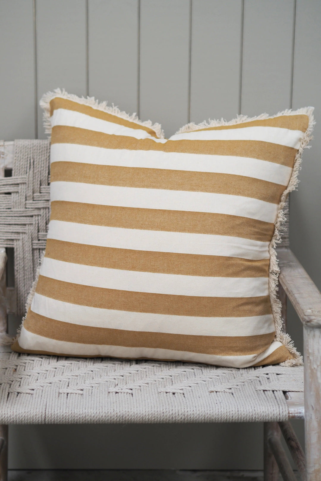 Striped pillow with brown and white stripes on a wicker chair against a gray wall.