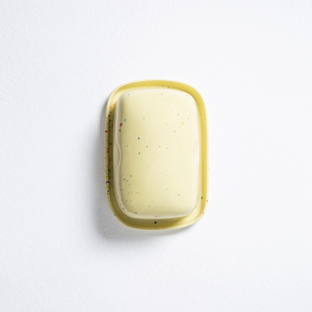Rectangular soap with speckled pattern in a yellow dish on a white background