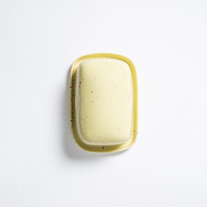 Rectangular soap with speckled pattern in a yellow dish on a white background