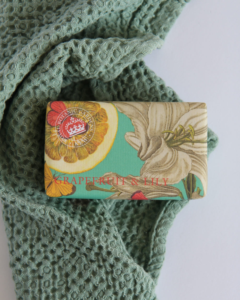A bar of Kew Botanical Soap with Grapefruit & Lily design, placed on a knitted green fabric.